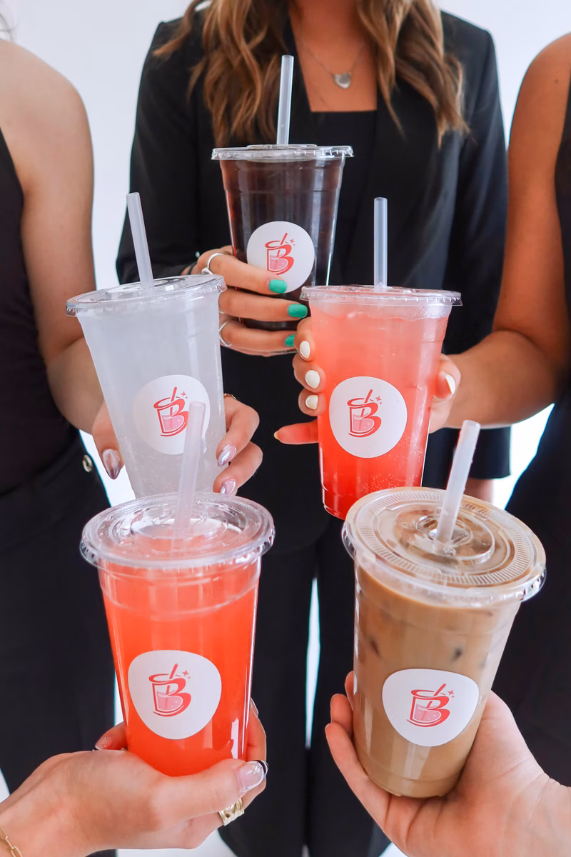 A hand holding up a signature The Bev drink against a sunny backdrop